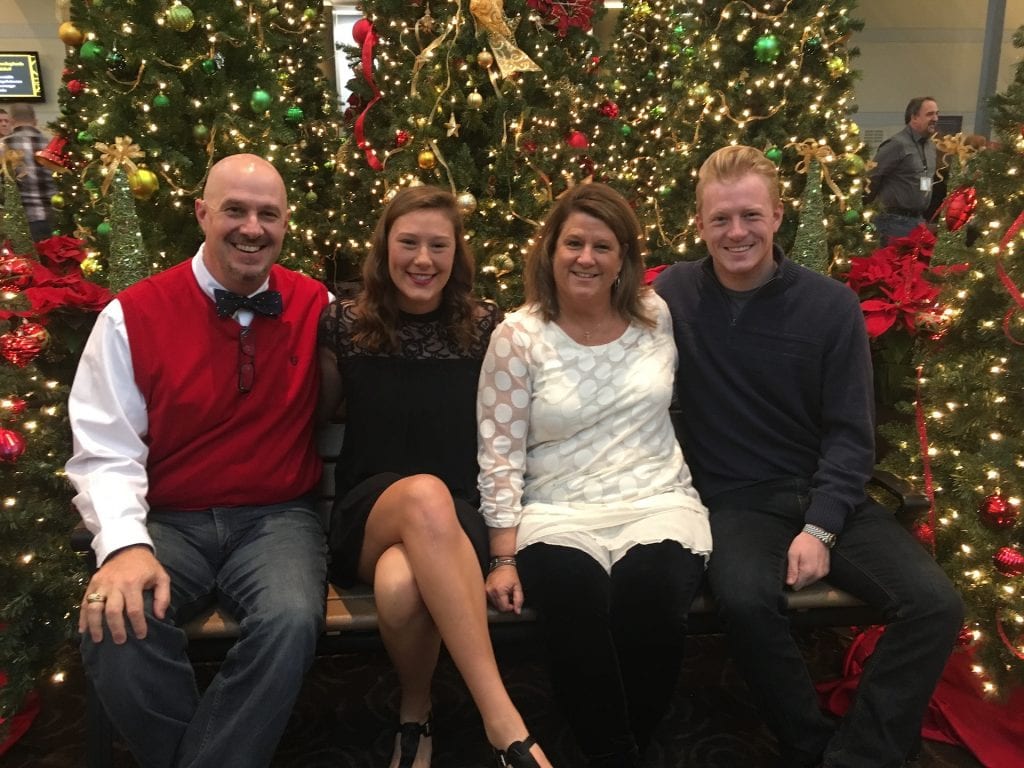 Megan and her mom, dad and brother pose in front of several decorated Christmas trees. 