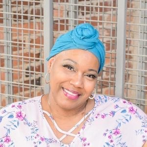 An African American breast cancer survivor named Felicia Robison smiles and radiates joy and positivity while wearing a teal head covering. 