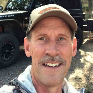 Greg Muhonen, prostate cancer survivor smiles in front of a black jeep rubicon