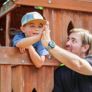 Eric Newman, founder of Roc Solid Foundation, smiles while giving a kid a high five on a playset that his organization built. 