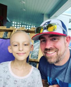 Eric Newman, the founder of Roc Solid Foundation, poses next to a kid with cancer whose head is bald. 