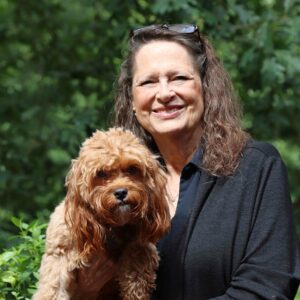 Maggie Bruehl, author and multiple myeloma survivor, smiles with her fluffy brown dog, Kassie. 